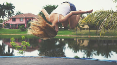 A woman doing a front flip on a trampoline, her long hair trailing behind.